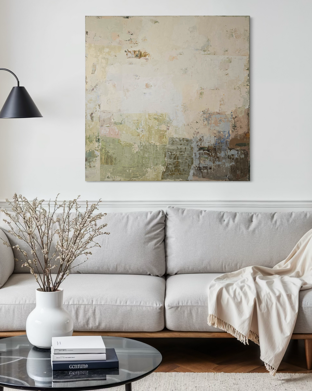 Modern living room with a light gray sofa, abstract painting in light tones, warm, beige colors, and decorative items.