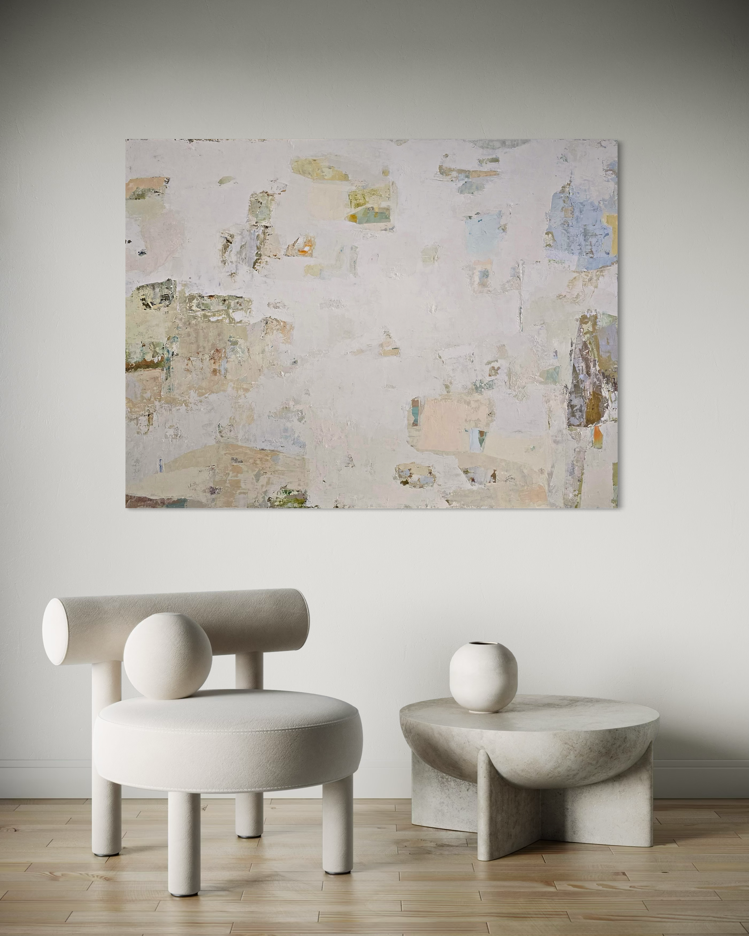 An abstract canvas painting with textured beige, white, and muted blue tones hangs on a light gray wall above a modern minimalist room setup featuring a round upholstered chair, a sculptural side table, and a small vase.