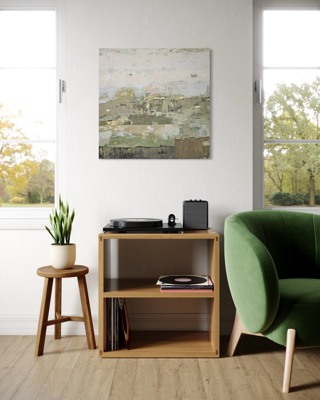 An abstract canvas painting created by Birute Studio in muted green, beige, and gray tones hangs on a white wall in a bright, modern living room. Below the painting is a light wood shelf holding a turntable, records, and a small speaker, next to a green armchair and a small wooden stool with a potted plant.