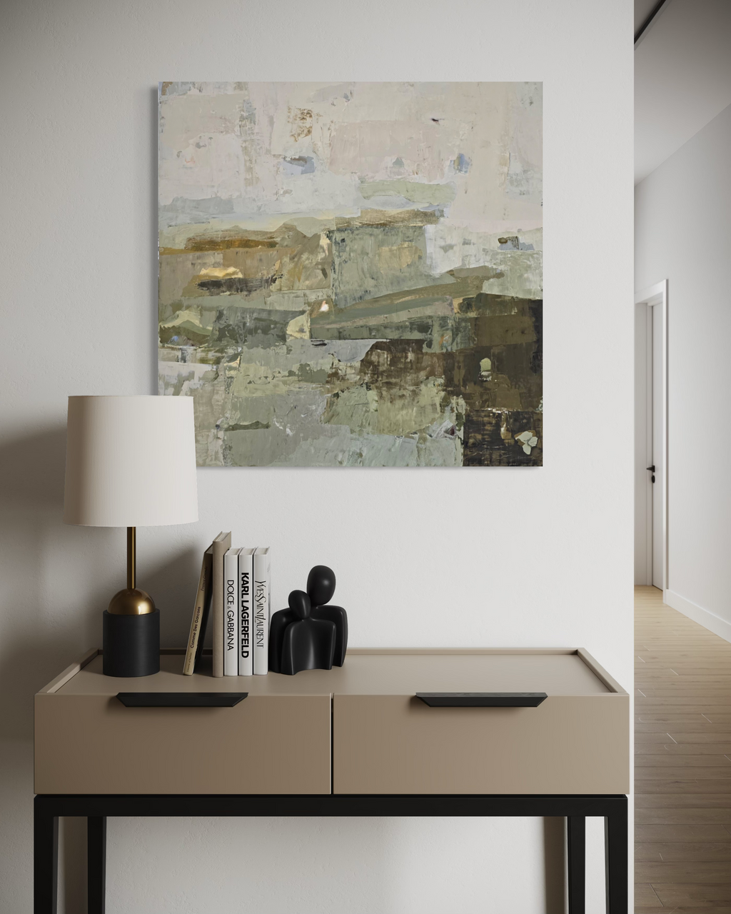 An abstract canvas painting created by Birute Studio in muted beige, gray, and olive tones hangs on a white wall above a console table with a lamp, books, and small black figurines.