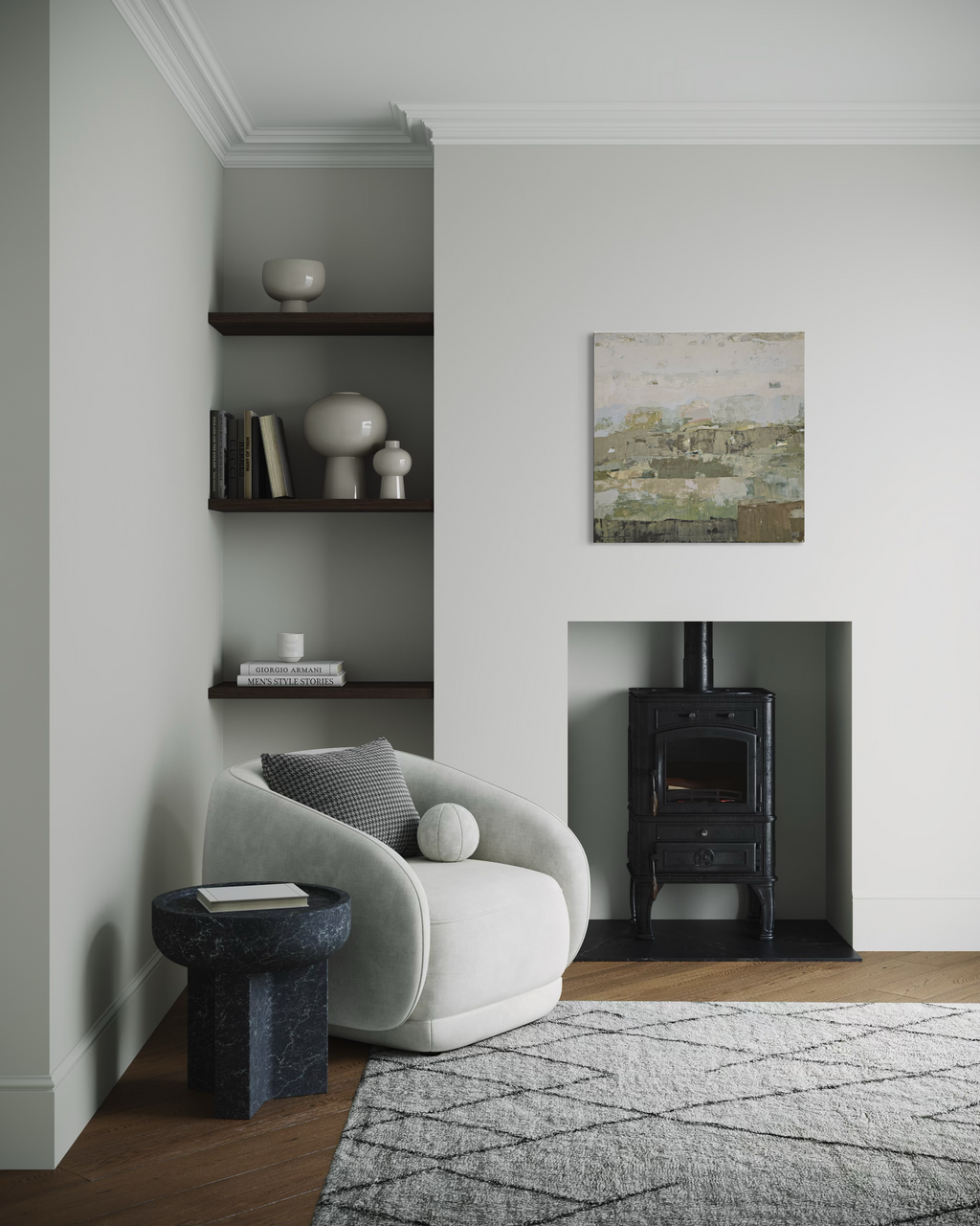 A styled interior corner featuring a light gray upholstered accent chair beside a dark marble side table, with built-in dark wood shelves, a black wood-burning stove in a fireplace niche, and a small landscape painting on the wall.