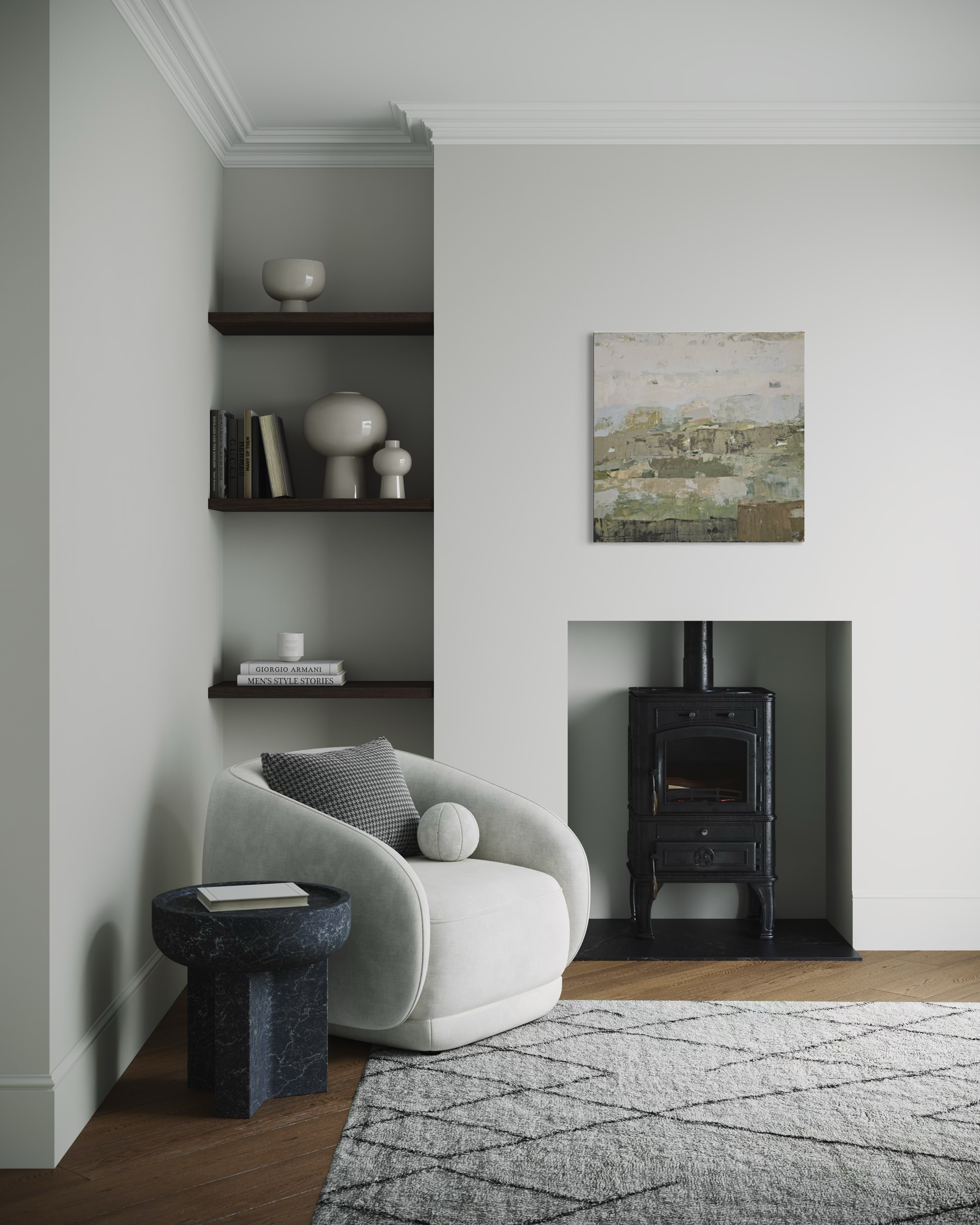A styled interior corner featuring a light gray upholstered accent chair beside a dark marble side table, with built-in dark wood shelves, a black wood-burning stove in a fireplace niche, and a small landscape painting on the wall.